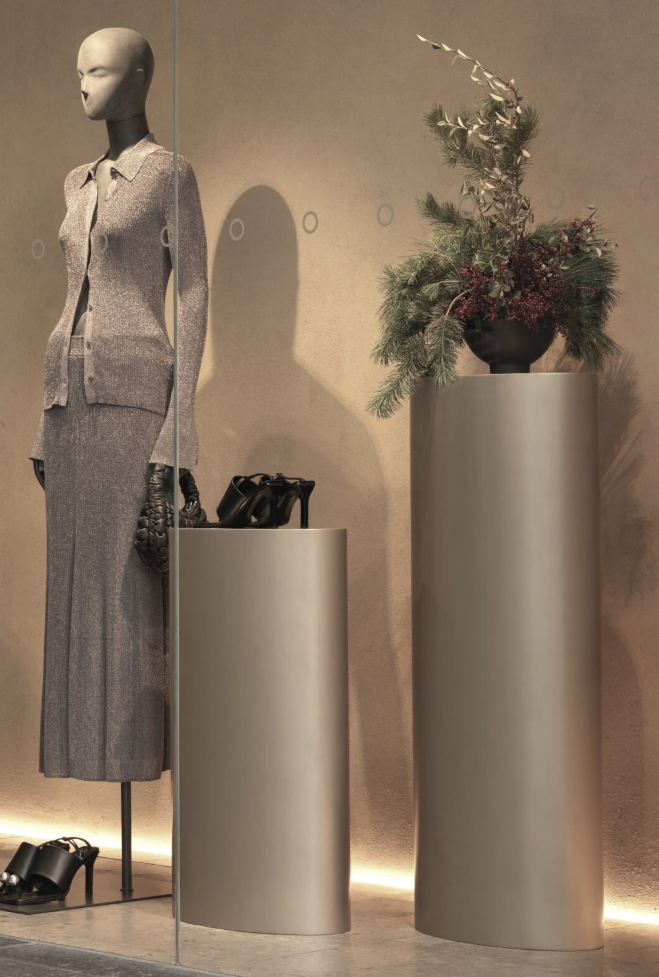 2 grey podiums, one with flowers on it and one with shoes on it next to a mannequin