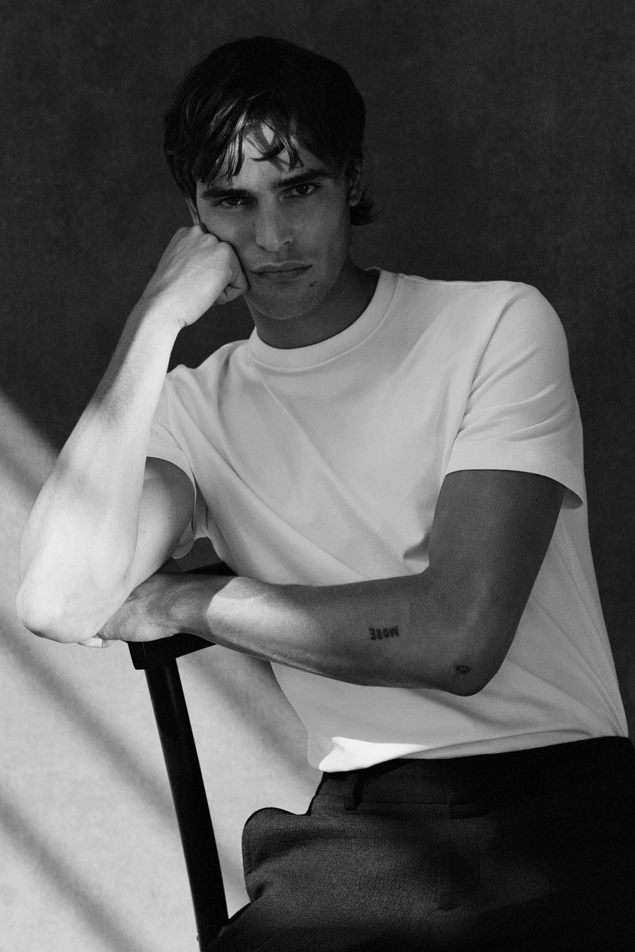 Man wearing white t-shirt and trousers whilst sitting on a chair