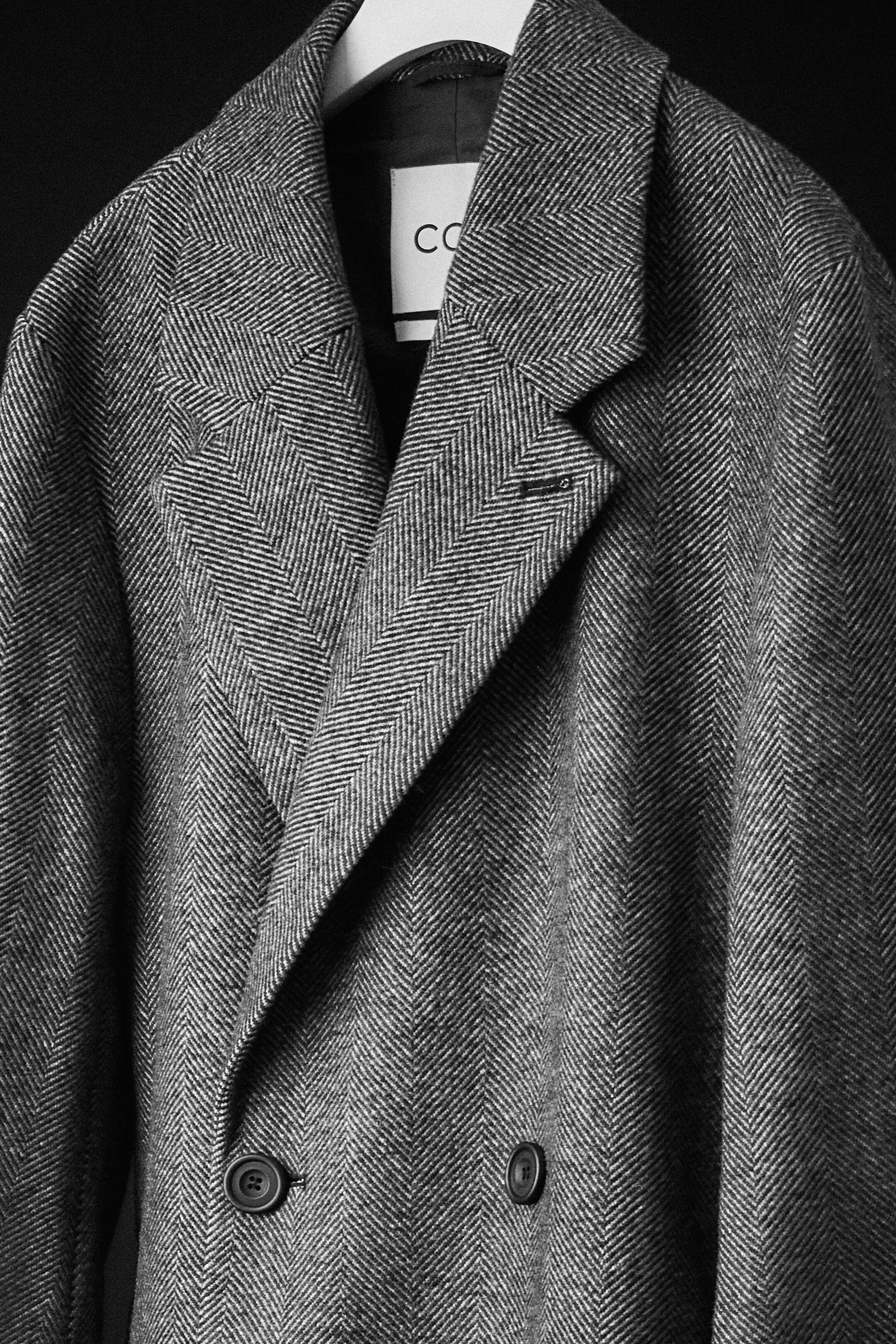 Black and white image of wool herringbone coat on a coat hanger