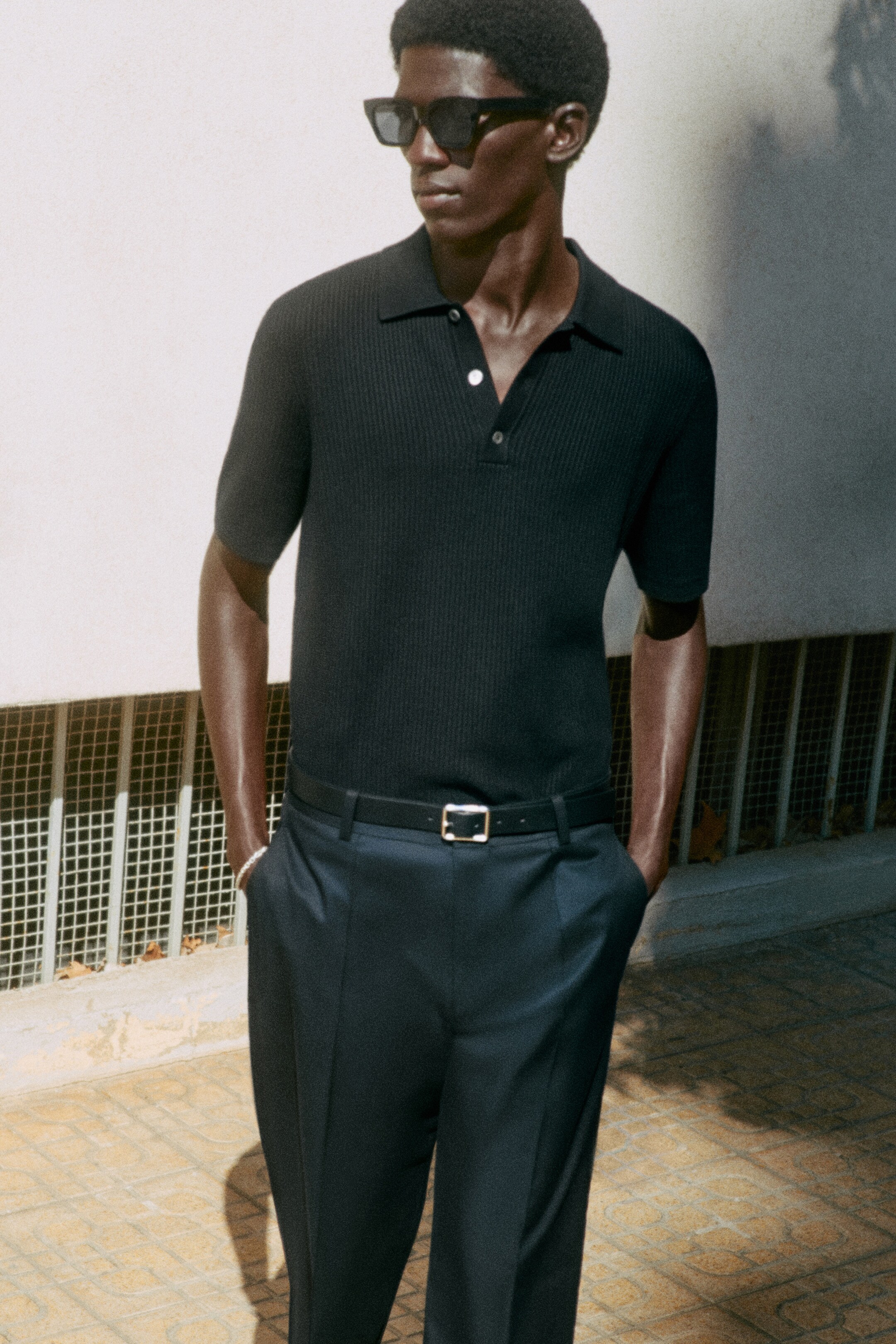 Man wearing black knitted polo top and navy trousers