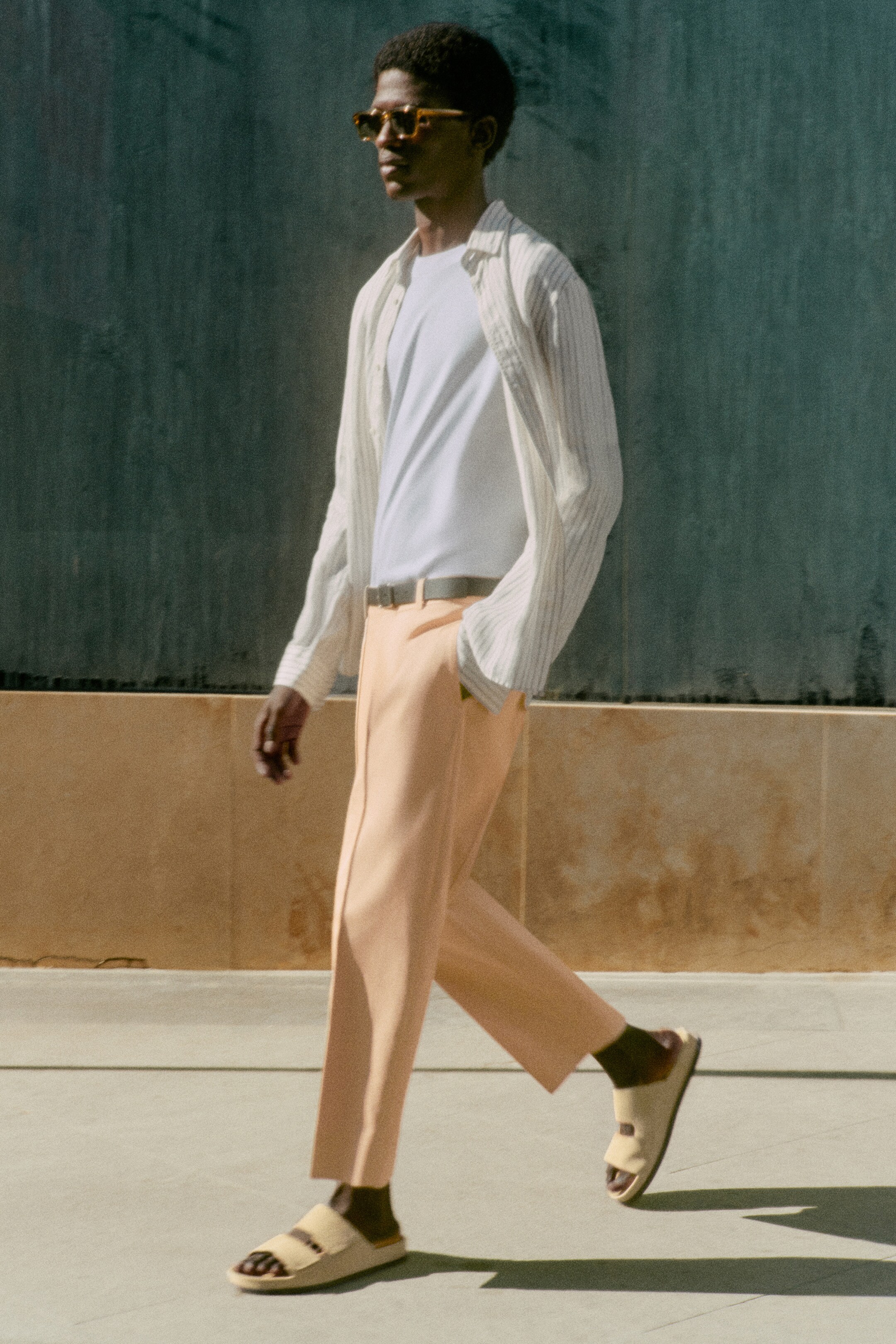 Man wearing open striped shirt with white tshirt underneath and coral trousers