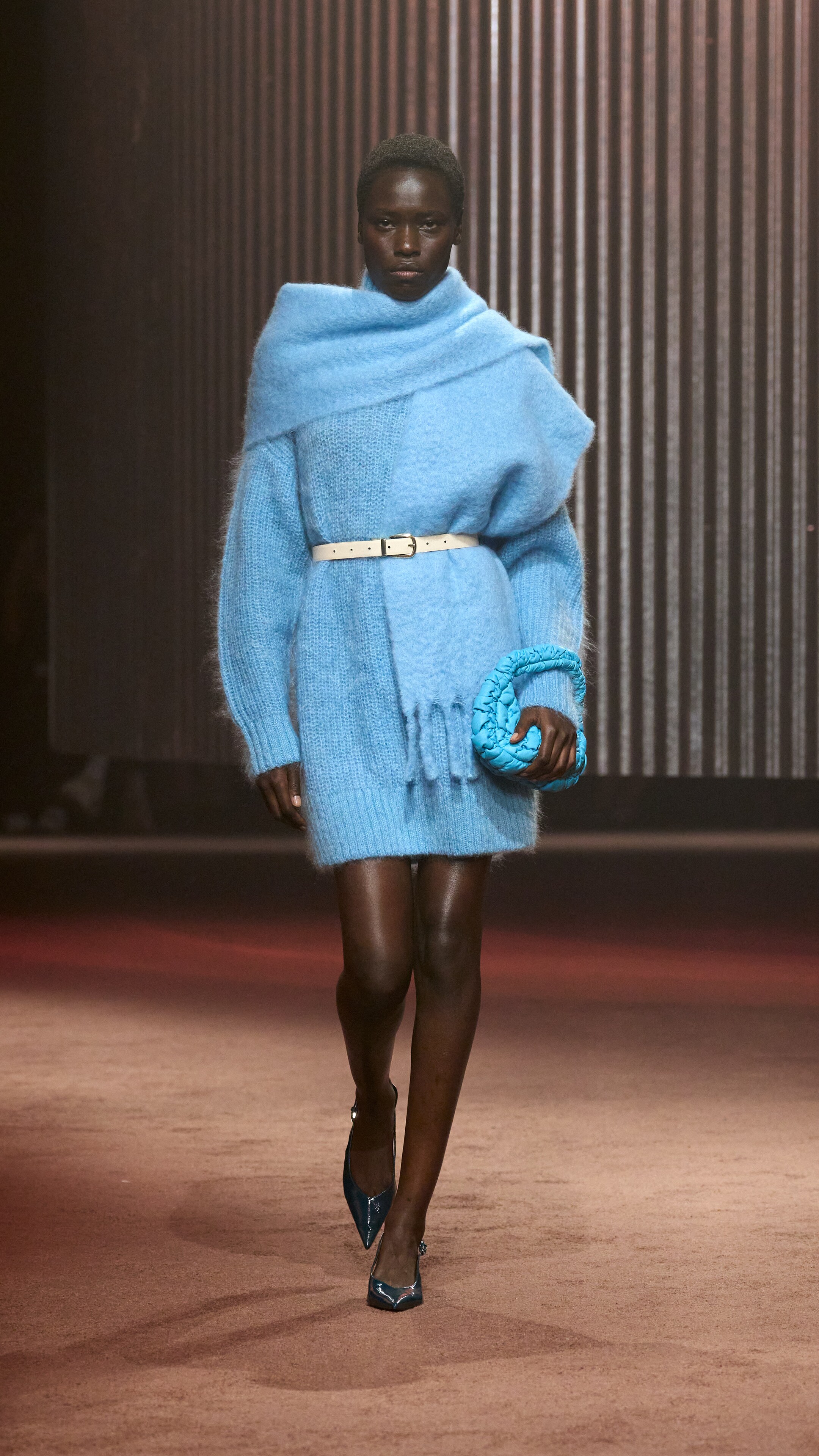 Woman wears blue knitted dress, blue scarf and carries blue bag