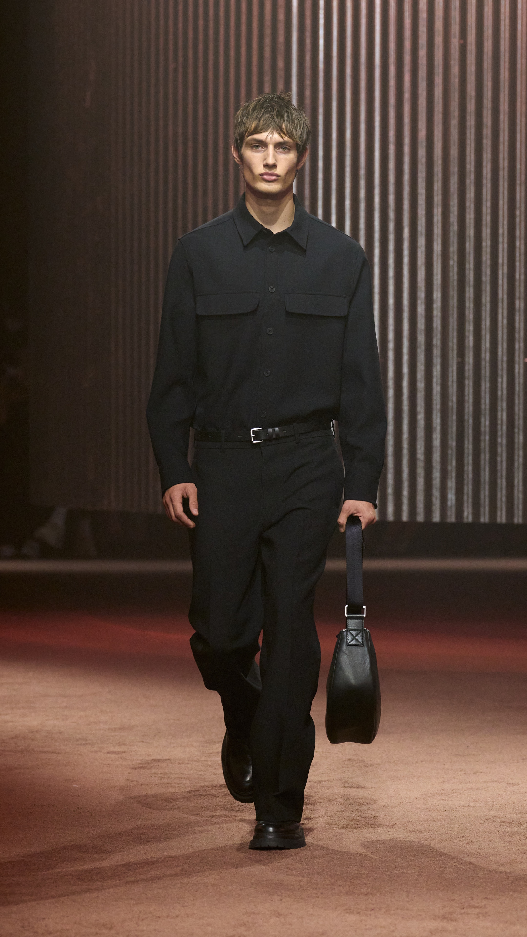 Man wears black shirt, black pants and holds black bag