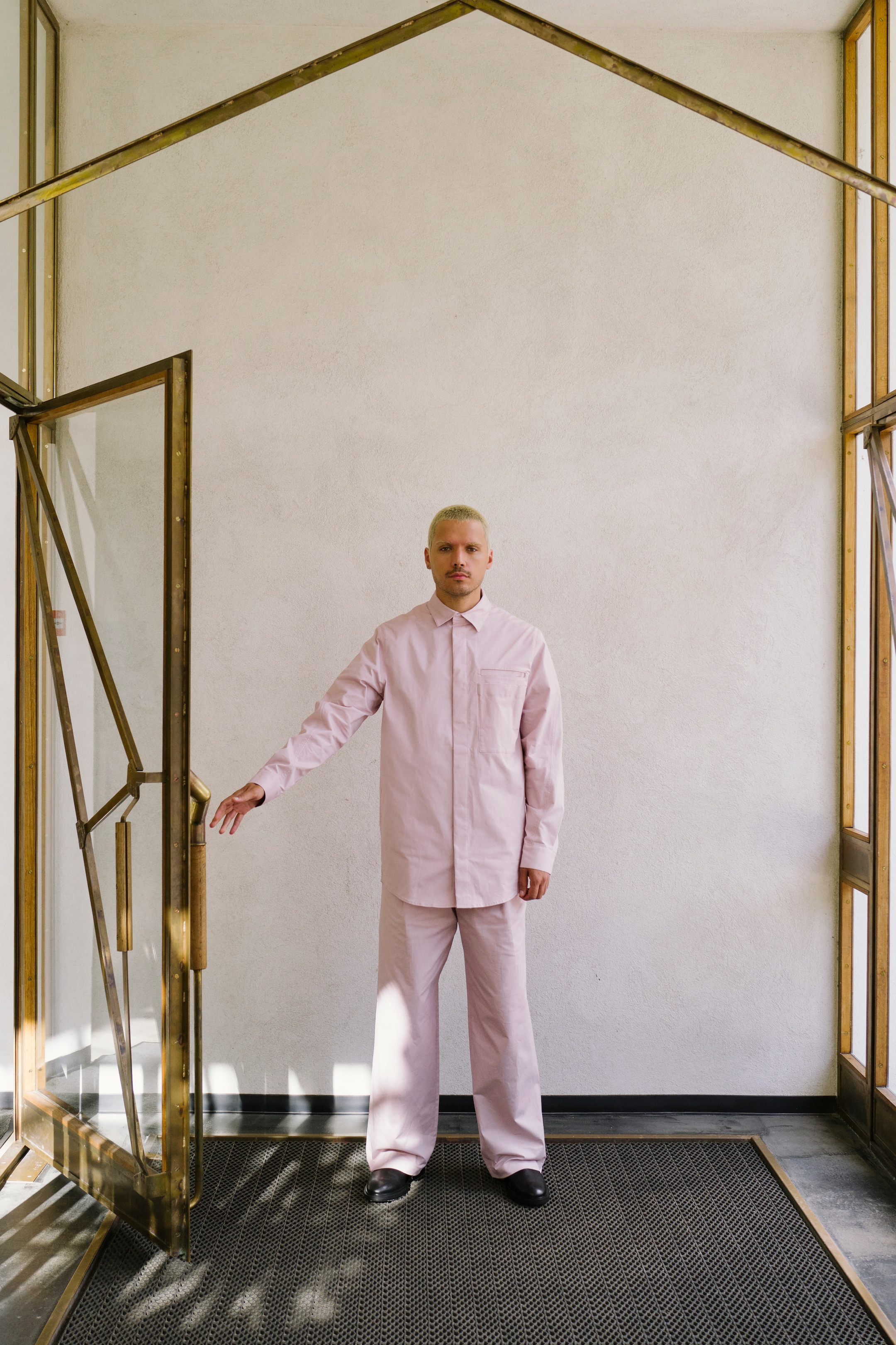 Harry Nuriev stands wearing pink shirt, pink trousers and black shoes