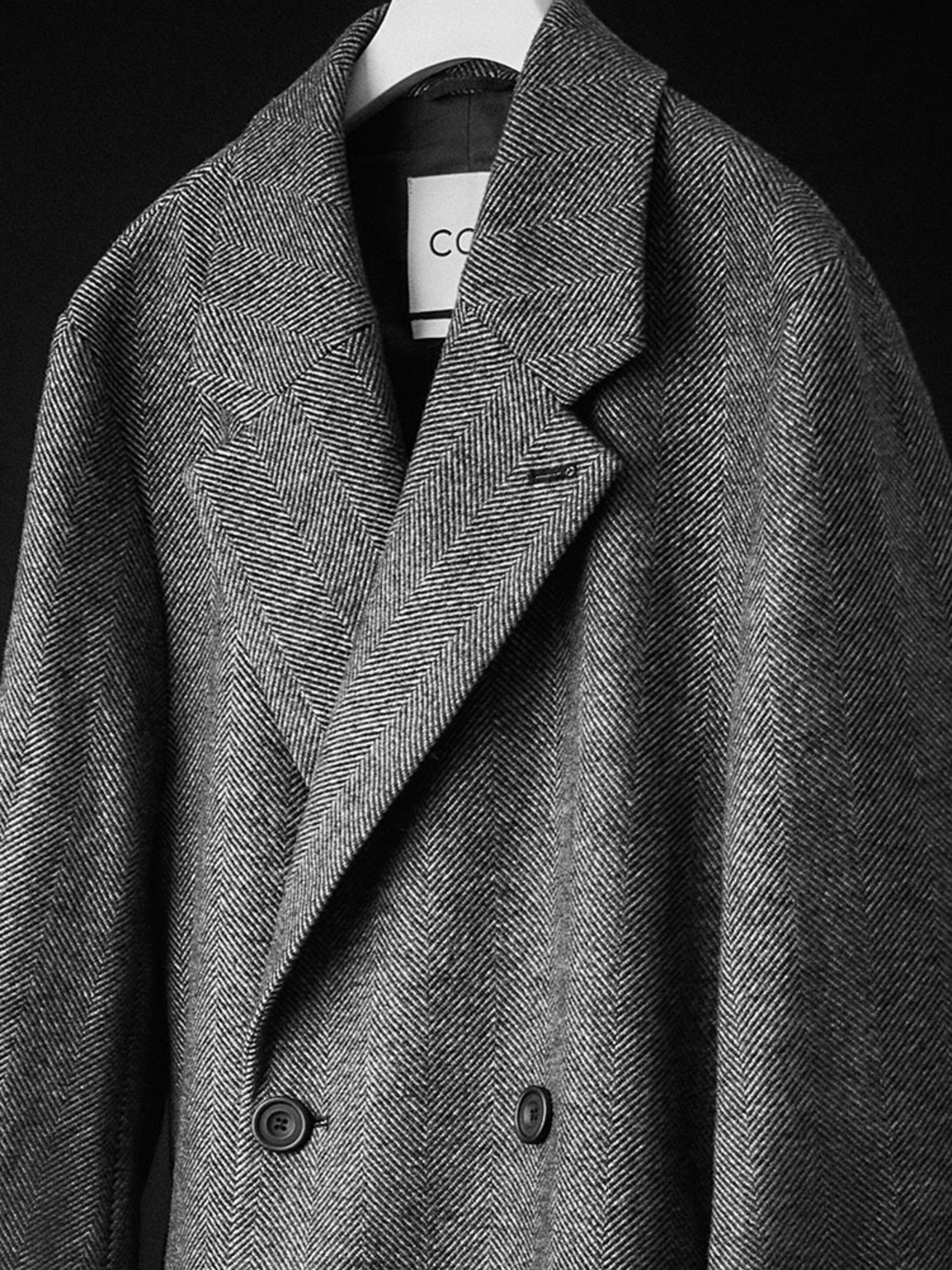 Black and white image of a herringbone coat hanging