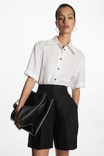 Placeholder for: Women wearing linen blouse tucked in to black high waisted shorts